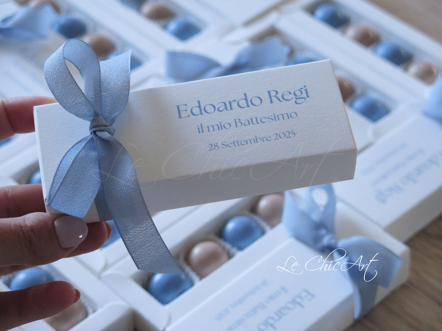 Vista ravvicinata scatole porta confetti battesimo con fiocco chiffon azzurro polvere, design minimalista sofisticato per cerimonie di classe