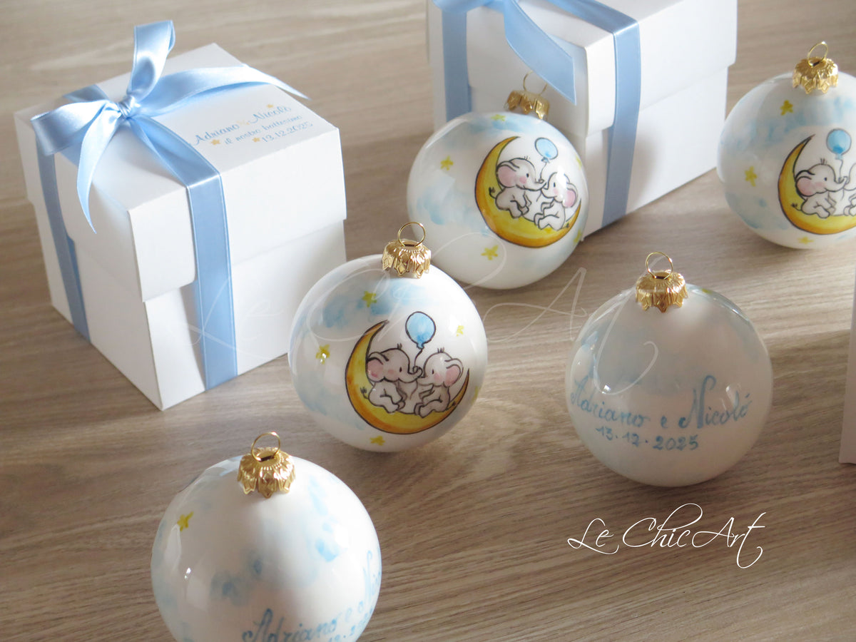 Bomboniere per due fratelli gemelli con elefantini dipinti a mano sulla luna, personalizzazione sul retro e scatole bianche con nastri azzurri.