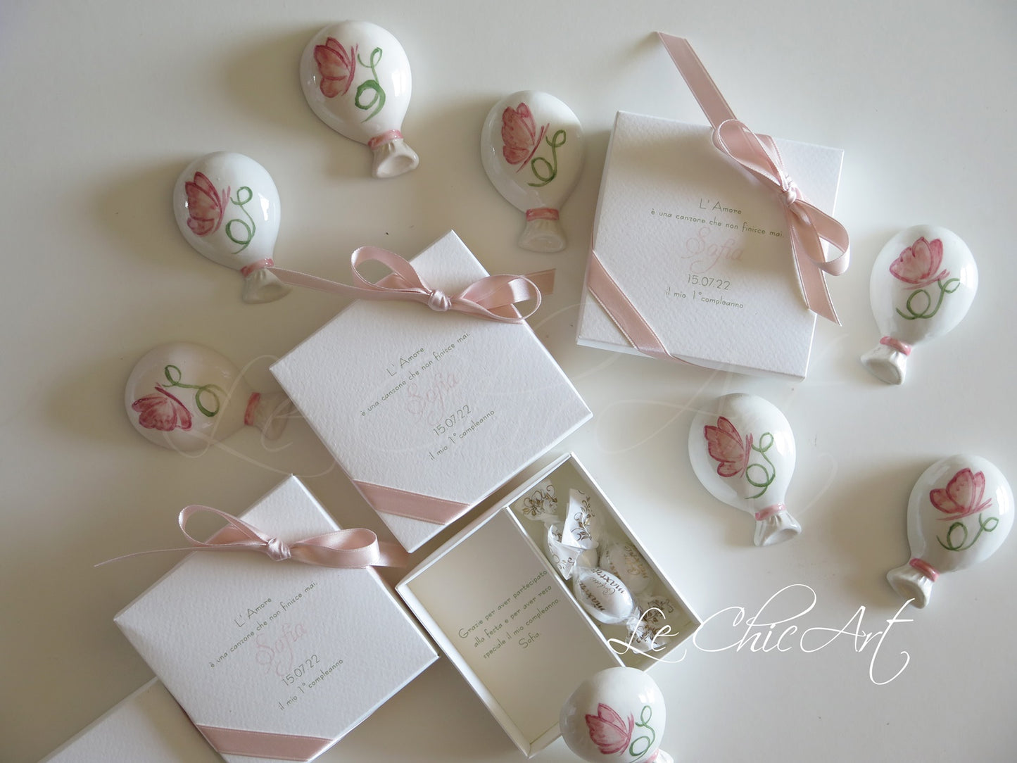 Dettaglio bomboniera palloncino ceramica bianca lucida dipinta a mano con farfallina rosa delicata e iniziale verde botanica, calamita integrata funzionale, bomboniera elegante per cerimonia battesimo o nascita