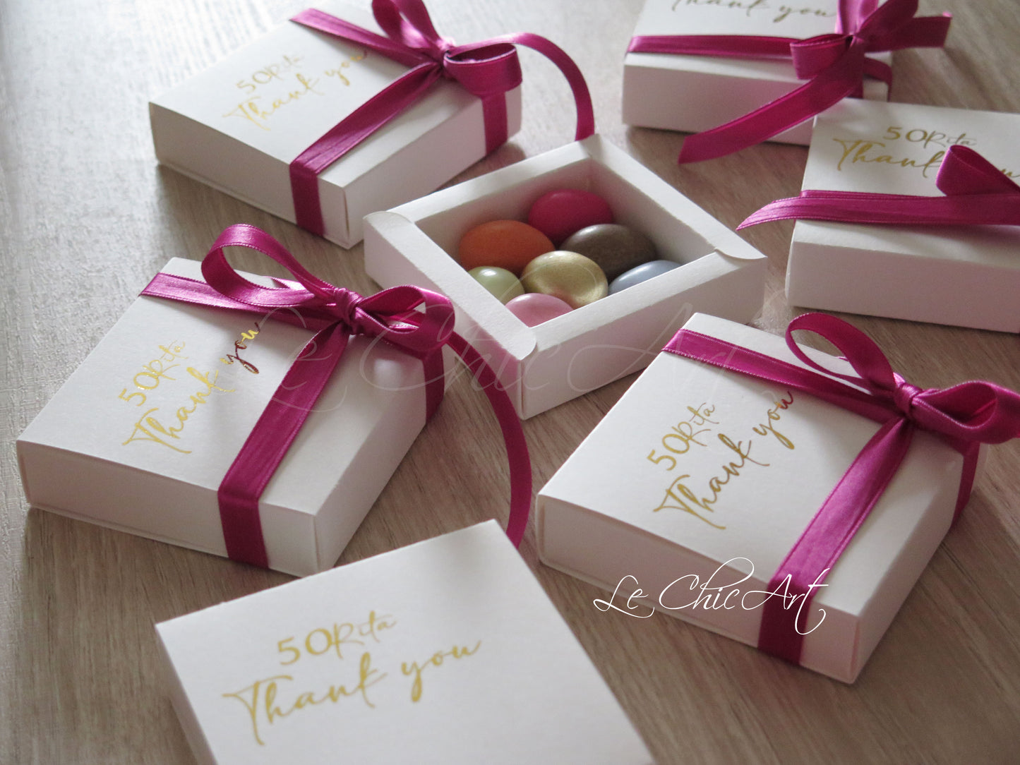 Scatola a sfilo fucsia 8x8x2cm aperta con confetti ripieni e nastro pretagliato per confezionamento facile bomboniera 50 anni