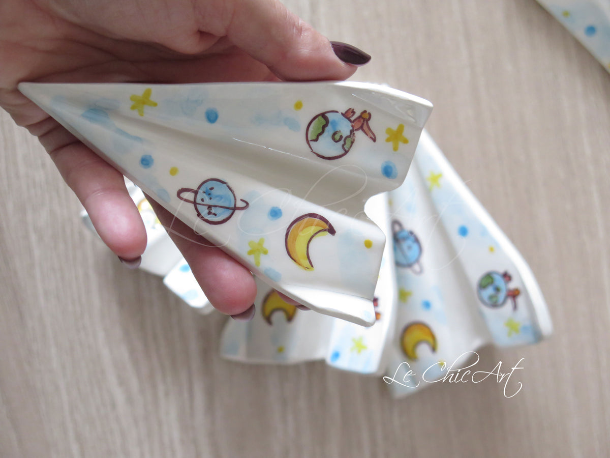 Dettaglio dell’aeroplano in ceramica dipinto a mano con Piccolo Principe sul pianeta, luna gialla, pianeta azzurro con anelli e stelline.