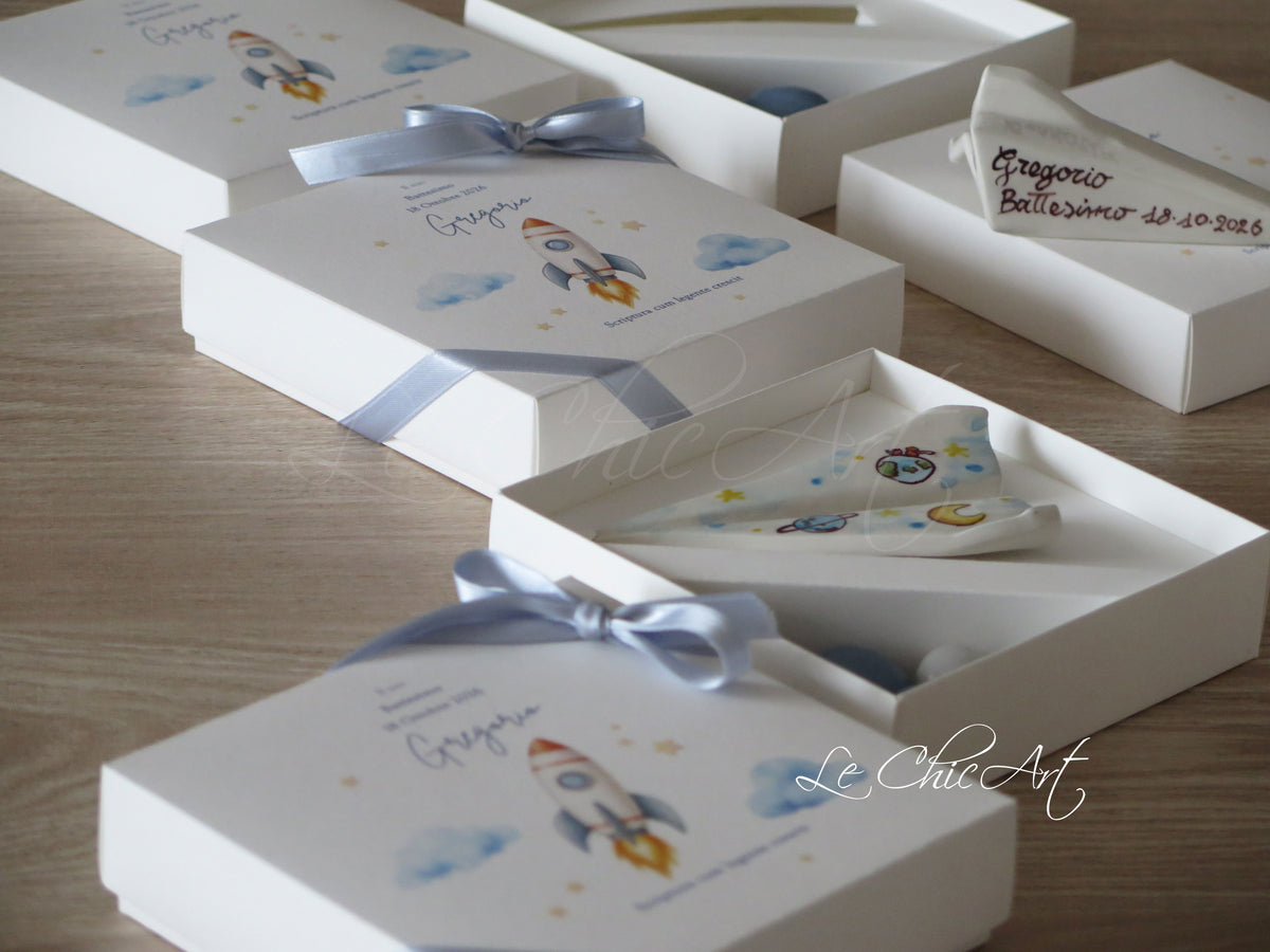 Scatole personalizzate con stampa razzo e fiocco azzurro, accanto agli aeroplani dipinti a mano per il Battesimo.