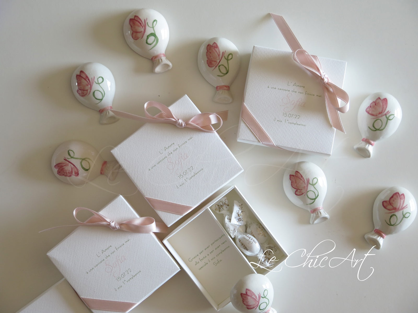 Dettaglio bomboniera palloncino ceramica bianca lucida dipinta a mano con farfallina rosa delicata e iniziale verde botanica, calamita integrata funzionale, bomboniera elegante per cerimonia battesimo o nascita
