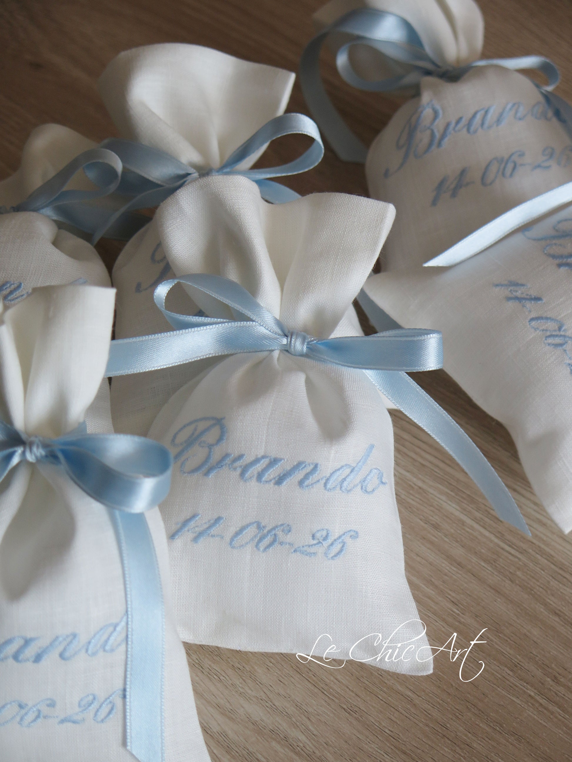 Sacchetti sartoriali in puro lino bianco con ricamo nome e data in calligrafia corsiva azzurro polvere, nastro doppio raso azzurro a fiocco, bomboniera battesimo Made in Italy Le ChicArt Lab